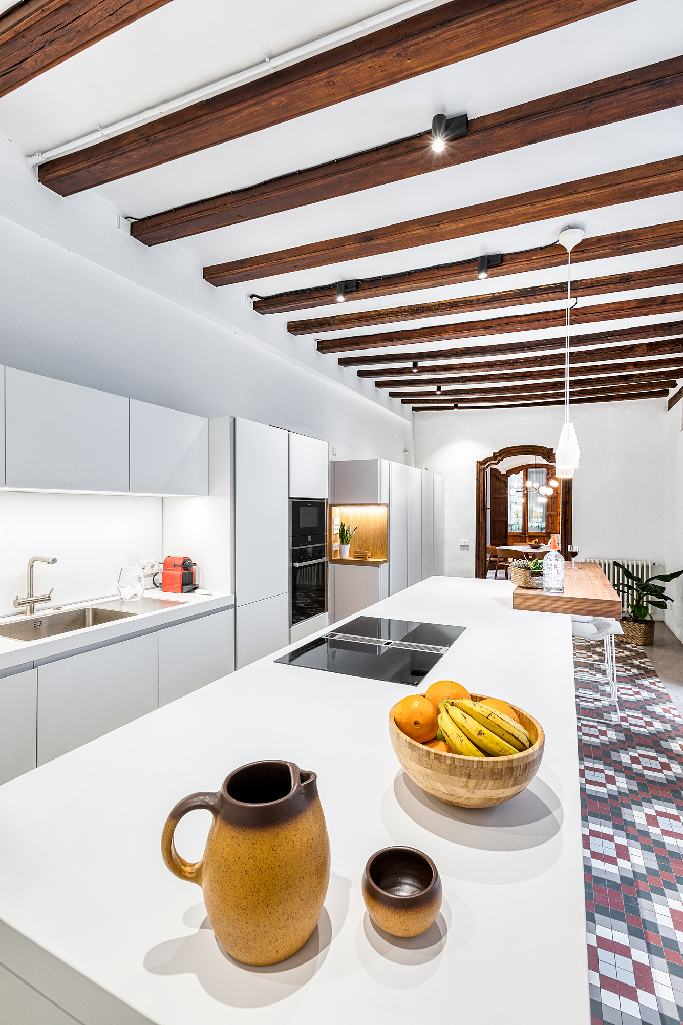 Modern kitchen featuring sleek cabinetry, a kitchen island, and rustic wooden beams overhead, located in a historic Barcelona home.