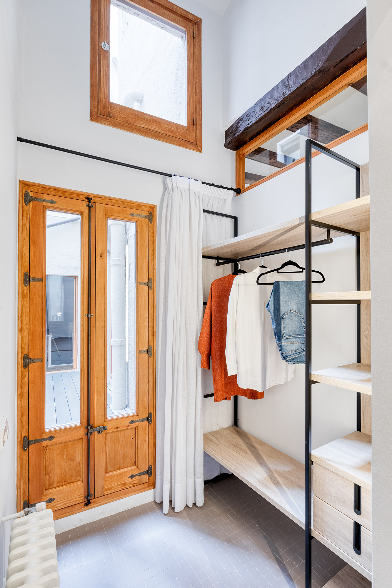 Bright and modern wardrobe area featuring wooden windows, light-colored walls, and a minimalist shelving unit with clothing hangers.