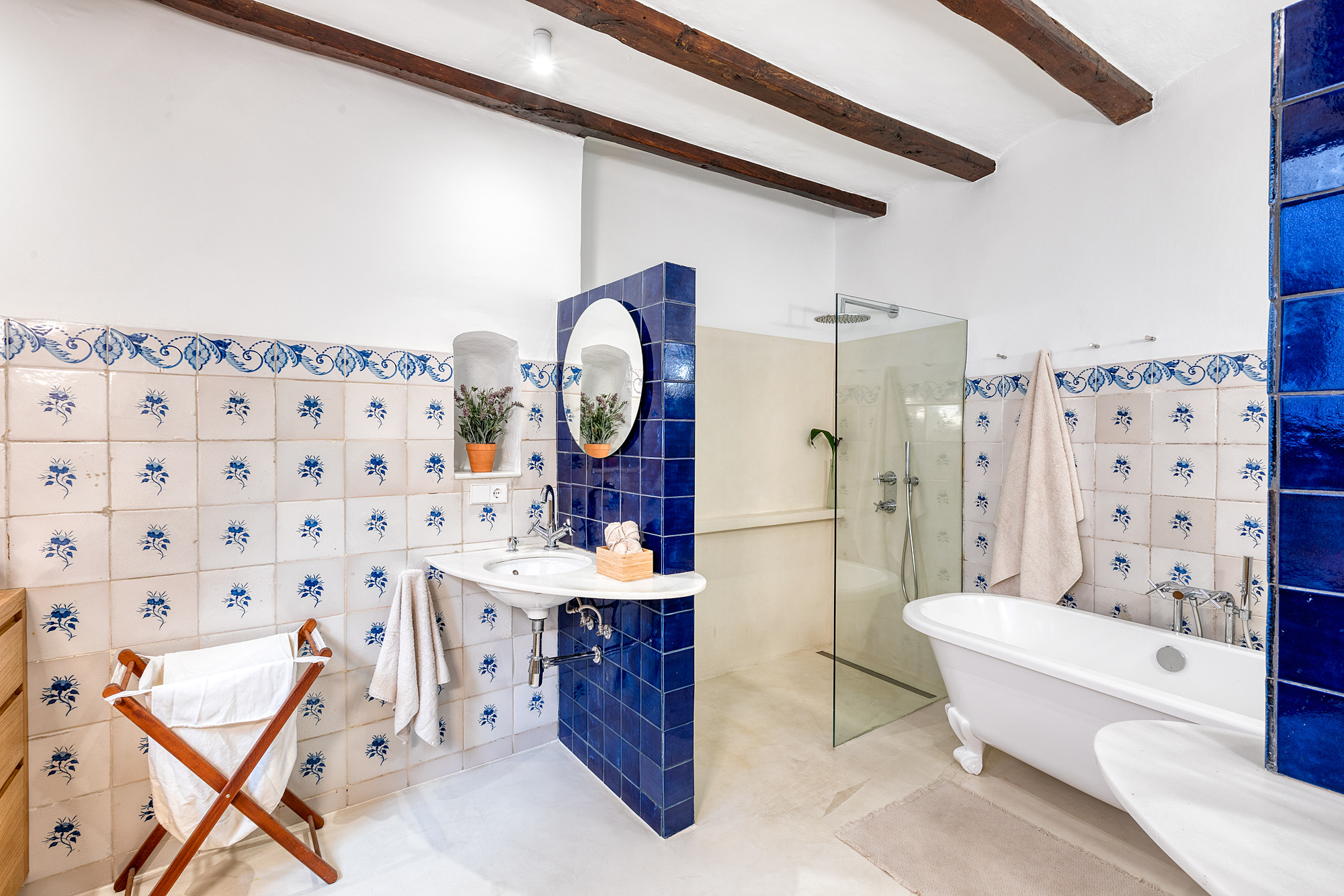 Bright and stylish bathroom featuring blue and white patterned tiles, a freestanding bathtub, a glass shower, and wooden beams overhead.