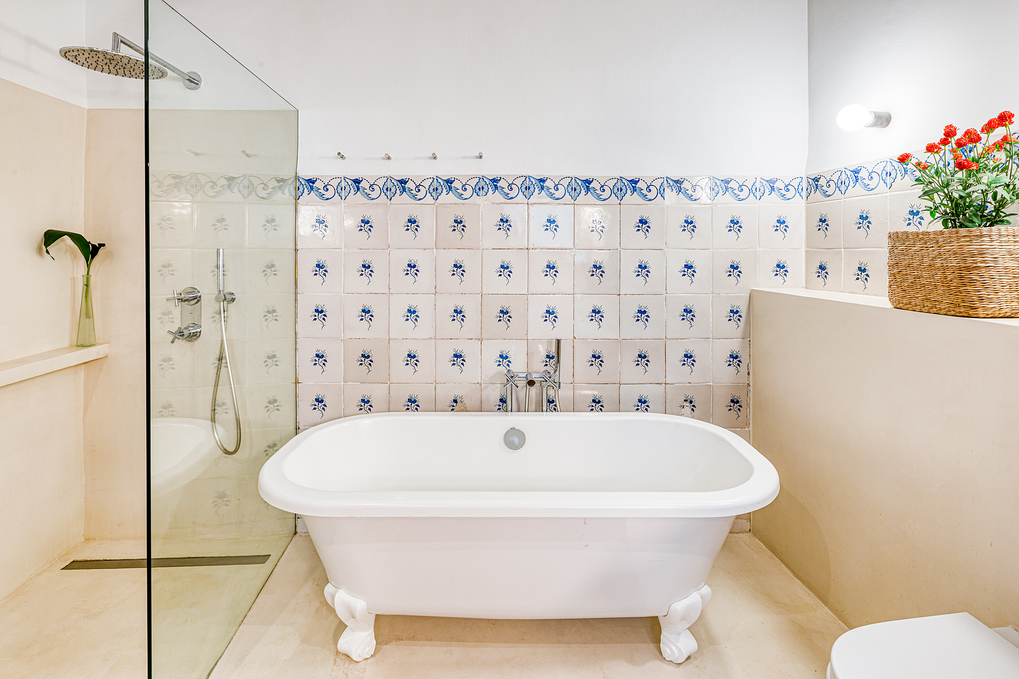 Bright bathroom featuring a freestanding white bathtub, walk-in shower with glass enclosure, and decorative tiles with floral patterns on the walls.