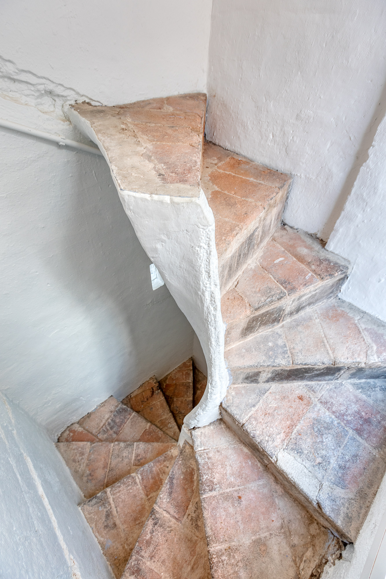Spiral staircase with terracotta steps and white walls in a historic Barcelona building.