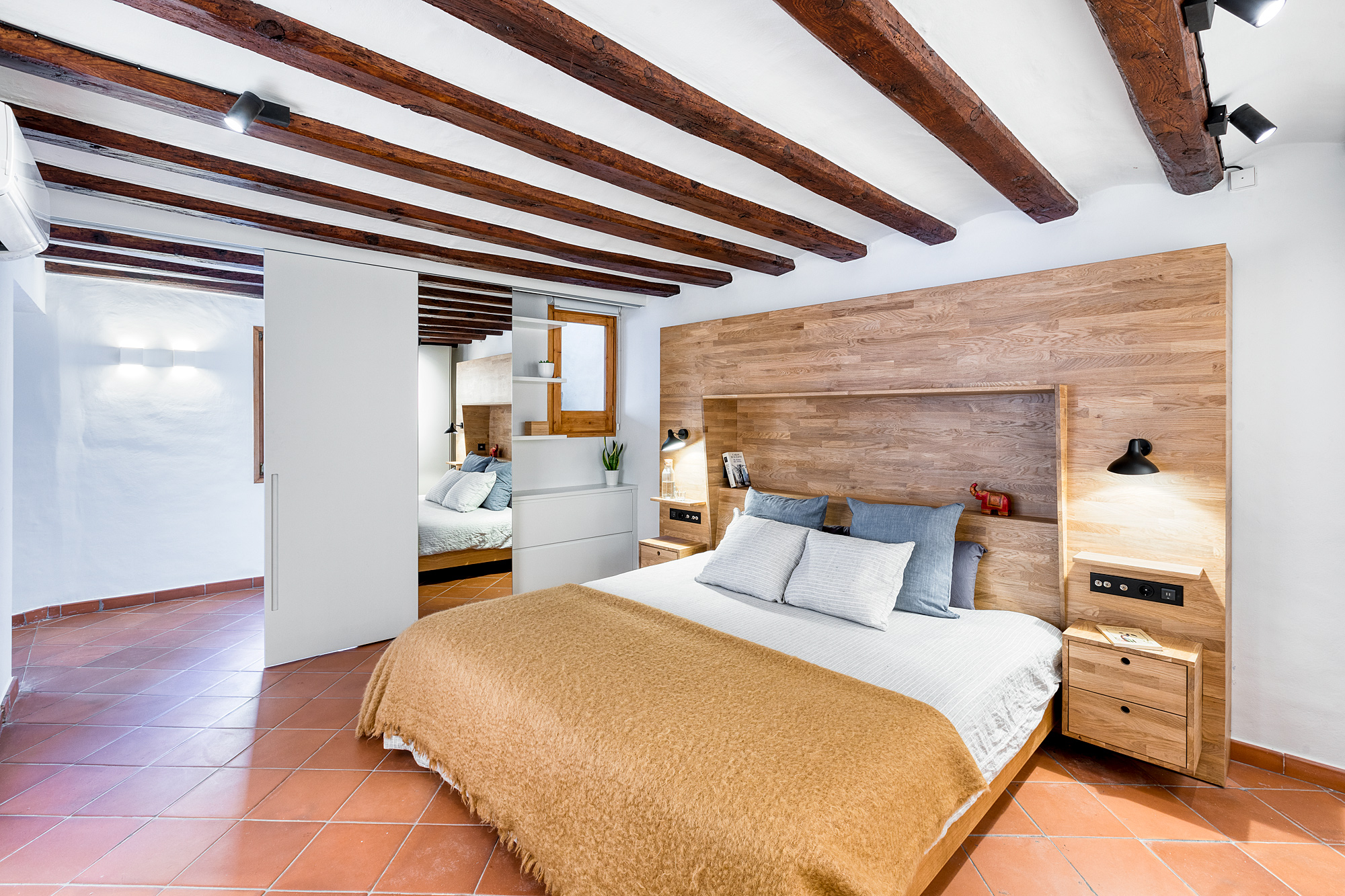 Cozy bedroom in a 17th-century palace featuring wooden beams, a beige blanket on the bed, and modern decor.